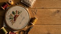 Embroidery hoop with floral needlework on linen fabric surrounded by colorful threads and sewing supplies on rustic wooden table for crafting projects.