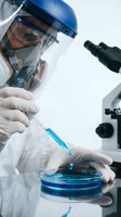 Scientist in protective equipment conducting laboratory research with syringe and petri dish for medical testing and pharmaceutical development.