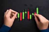 Hands arranging red and green candlestick chart pattern showing market trends and stock price movements on dark background, financial trading concept.