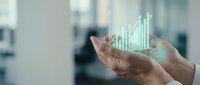 Male professional hands holding holographic growth chart with upward trending bars in modern office setting for business analytics and financial success concepts.