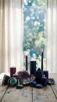 Elegant candle arrangement with amethyst crystals and gemstones on wooden surface near window with soft natural light creating peaceful meditation atmosphere.