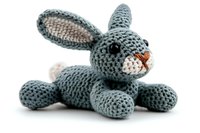 Gray knitted bunny rabbit toy with long ears and pink nose lying on white background, handmade amigurumi crochet plush animal isolated for craft and design use.