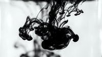 Black ink swirling and dispersing in clear water creating abstract fluid patterns and organic shapes for artistic design projects.
