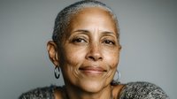 Close-up portrait of mature African American woman with short gray hair and hoop earrings, smiling gently against neutral background.