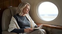 Elegant blonde businesswoman relaxing in luxury private jet cabin, looking out window during flight. Corporate travel and executive lifestyle concept.