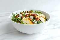 Fresh pear and blue cheese salad with toasted pecans and arugula in white ceramic bowl on marble surface, appetizing healthy lunch option.
