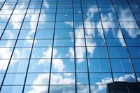 Modern glass facade of office building reflecting blue sky and white fluffy clouds, creating geometric pattern of windows. Corporate architecture background.