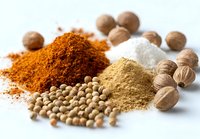 Aromatic spices and herbs collection with colorful powders, whole nutmeg, coriander seeds, and ground seasonings on white background.