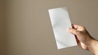 Hand holding blank white rectangular paper against neutral beige background, suitable for mockups, presentations, and advertising campaigns.