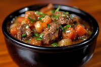 Hearty beef stew with tender meat chunks, carrots and potatoes in rich brown gravy, garnished with fresh herbs in black ceramic bowl on wooden surface.