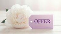 White peony flower beside a lavender price tag with the word Offer on a soft wooden background, evoking elegance and spring promotions.