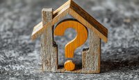 Wooden house silhouette with orange question mark inside on textured gray background. Concept for real estate questions, property decisions and housing market uncertainty.