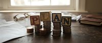 Wooden blocks spelling LOAN placed on stacks of coins with financial documents and glasses on desk, representing personal finance and lending concepts.