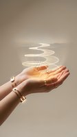 Female hands with gold jewelry holding glowing spiral light energy against neutral background representing magic, healing, and spiritual power.