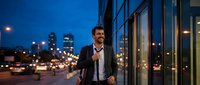 Professional businessman walking along modern glass building at night with city lights and traffic in urban downtown area for corporate lifestyle.