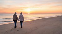 Senior couple walking hand in hand on beach at sunset, romantic golden hour moment, peaceful ocean waves, retirement lifestyle, love and togetherness.