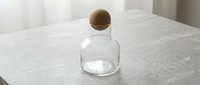 Transparent glass bottle with wooden spherical stopper on marble surface, suitable for cosmetics, perfume, or luxury product packaging and branding.