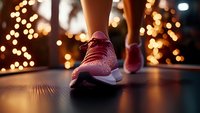 Pink athletic sneakers on female runner with blurred bokeh lights in background creating magical evening atmosphere for sports and fitness motivation.