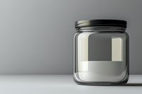 Empty glass jar with black metal lid on white surface against gray background, minimalist composition showing transparency and reflection.