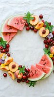 Summer fruit wreath with watermelon slices, cherries, peaches, and mint on white linen, flat lay food styling for seasonal design.