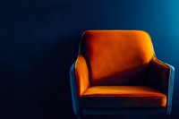 Orange velvet armchair illuminated dramatically against dark blue background, creating modern minimalist composition with strong contrast and moody atmosphere.