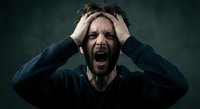 Stressed Caucasian man screaming with hands on head expressing mental breakdown, anxiety and emotional crisis against dark moody background.
