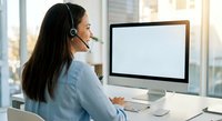 Professional Asian businesswoman with headset working at computer in modern office environment for customer service and remote work applications.