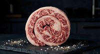 Raw marbled beef roll sliced on dark slate board with peppercorns and salt crystals for gourmet cooking and culinary presentations.