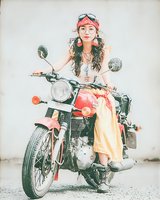 Young woman with long curly hair wearing red bandana and goggles sitting on vintage motorcycle in artistic painterly style. Perfect for travel and adventure themes.