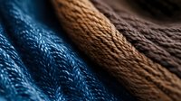 Textured knitted fabric in blue, brown, and dark brown colors arranged in soft folds, creating a cozy winter fashion background.