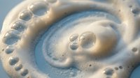 Creamy white foam swirl with bubbles on light blue background. Abstract soap lather spiral pattern for cleaning, skincare and hygiene product concepts.