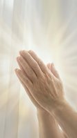 Elderly hands pressed together in prayer position with divine light rays streaming through soft background for spiritual and religious concepts.