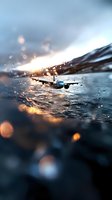 Commercial passenger aircraft flying low over stormy ocean water at sunset, with dramatic water droplets and bokeh light effects creating atmospheric mood.