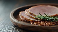 Sliced ham with rosemary sprig and scattered brown lentils on rustic wooden serving board against dark background, moody food photography styling.