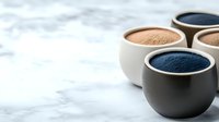 Minimalist ceramic bowls with natural mineral powder pigments in earthy blue and brown tones on marble surface, selective focus with copy space for cosmetics.