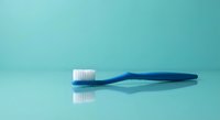 Blue toothbrush with white bristles on turquoise background. Dental hygiene and oral care concept for healthcare and wellness designs.