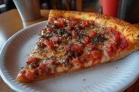 Fresh slice of pizza with melted mozzarella cheese, diced tomatoes and Italian herbs on crispy golden crust served on white disposable plate.