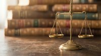 Golden scales of justice on wooden desk with vintage law books in blurred background. Legal concept for courtroom, attorney office, judicial system.
