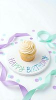 Vanilla cupcake with swirled frosting on a Happy Birthday plate, surrounded by pastel ribbons and confetti on white background.
