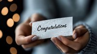 Hands holding glittery silver card with congratulations message against blurred bokeh lights background, perfect for celebration announcements.