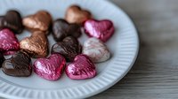 Assorted chocolate heart candies in foil wrappers on white plate for Valentine's Day celebration and romantic occasions.