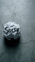 Crumpled paper ball with the word Sorry on a dark concrete floor, symbolizing regret, apology, and failed communication.