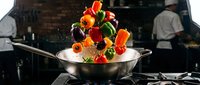Fresh colorful bell peppers and vegetables tossed in a steel wok on a gas stove in a professional restaurant kitchen.