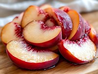 Fresh ripe peaches sliced and arranged on wooden cutting board, showcasing juicy flesh and vibrant red skin for culinary and food styling projects.