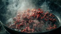 Sizzling ground meat browning in black cast iron pan with rising steam and smoke creating dramatic cooking atmosphere. Professional food preparation.