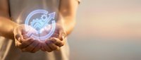 Hands holding a glowing holographic icon with gear, arrow, and growth chart symbolizing business productivity and innovation.