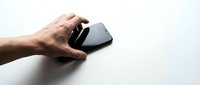 Male hand holding black wireless computer mouse on white surface, suitable for technology, business, and office design projects.