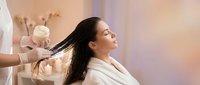 Young woman enjoying professional hair treatment at luxury spa salon with stylist applying care products for healthy shiny hair and relaxation.