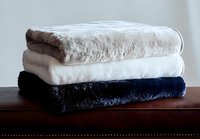 Stack of folded soft plush blankets in white, gray and navy blue colors on wooden surface against light background, cozy home textile arrangement.