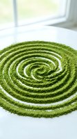 Vibrant green matcha powder arranged in concentric spiral pattern on white surface with natural window light, suitable for tea and wellness content.